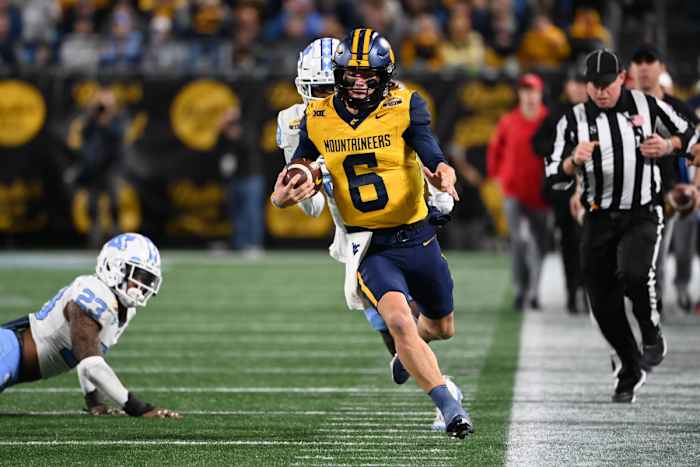 Dec 27, 2023; Charlotte, NC, USA; West Virginia Mountaineers quarterback Garrett Greene (6) with the ball as North Carolina Tar Heels linebacker Power Echols (23) and defensive back Marcus Allen (29) defend in the third quarter at Bank of America Stadium. Mandatory Credit: Bob Donnan-USA TODAY Sports